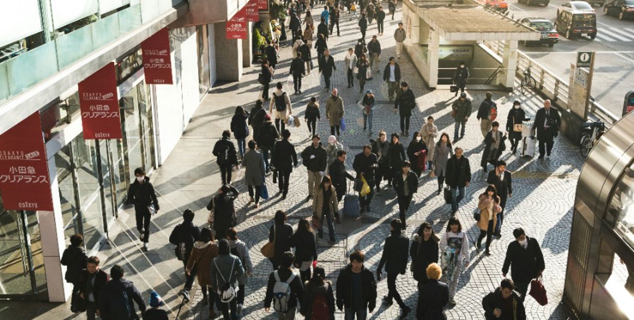 Solig stad med mycket folk som går åt olika håll.